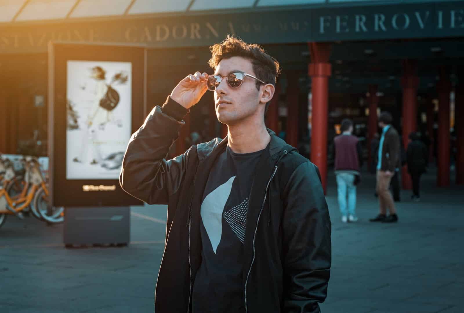Man in sunglasses and a black zip-up jacket outside a train station