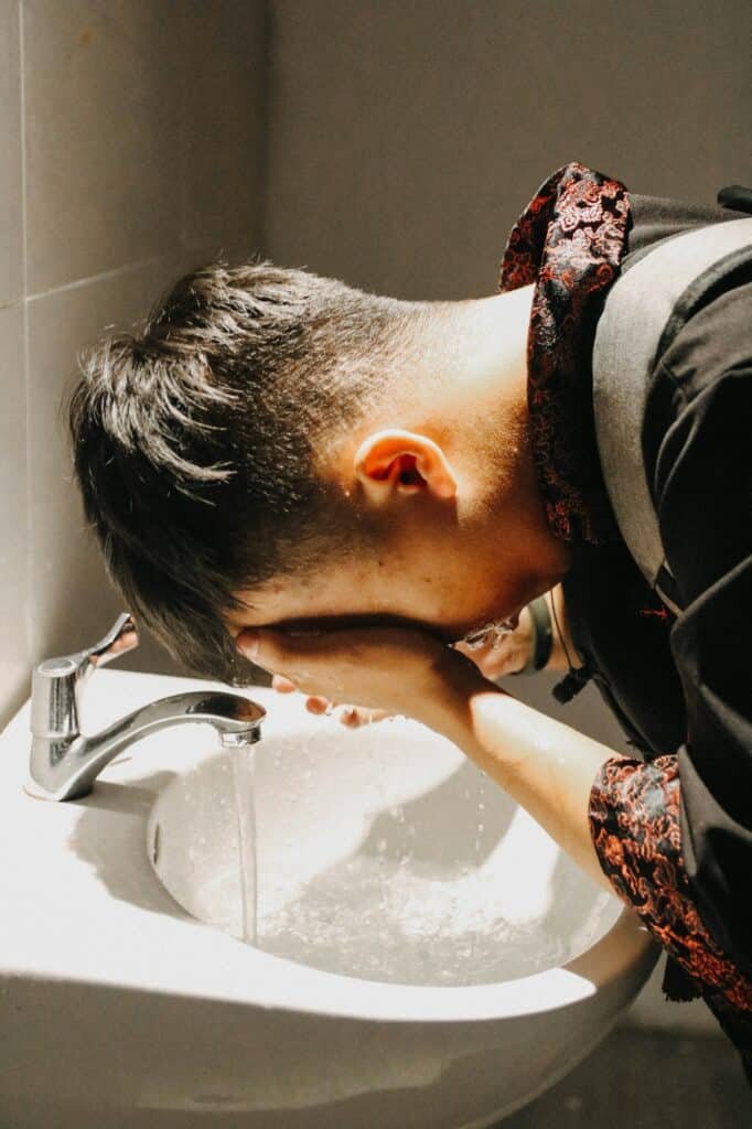 Man leaning over a sink washing his face