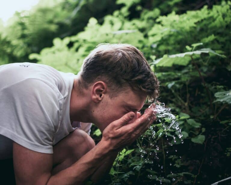 Man splashing water on his face outdoors among green leaves