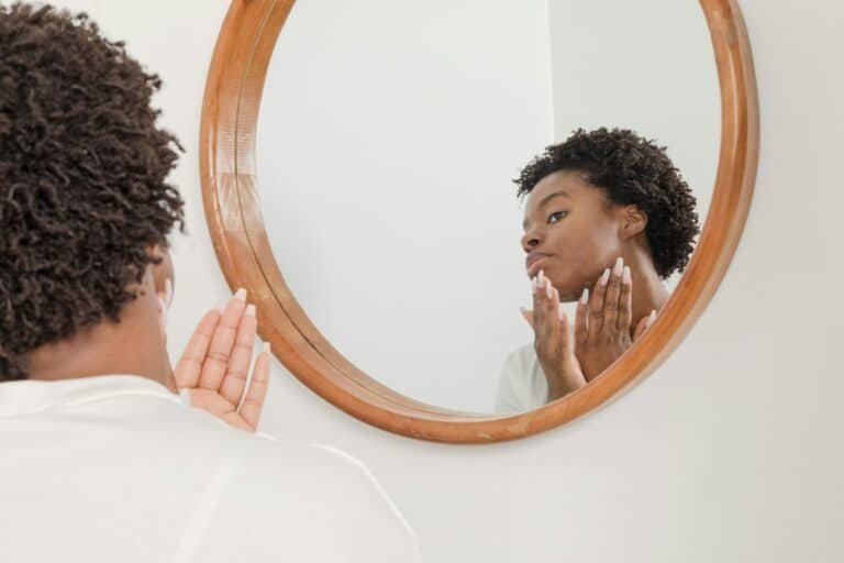 Man touching his face while looking into a round mirror