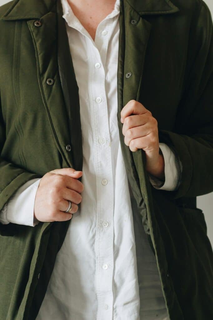 Close crop of an olive cotton coat worn open over a white button-up shirt