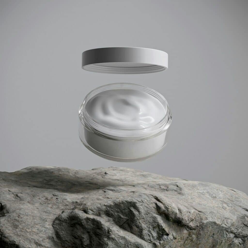 Open jar of white face cream floating above a rock