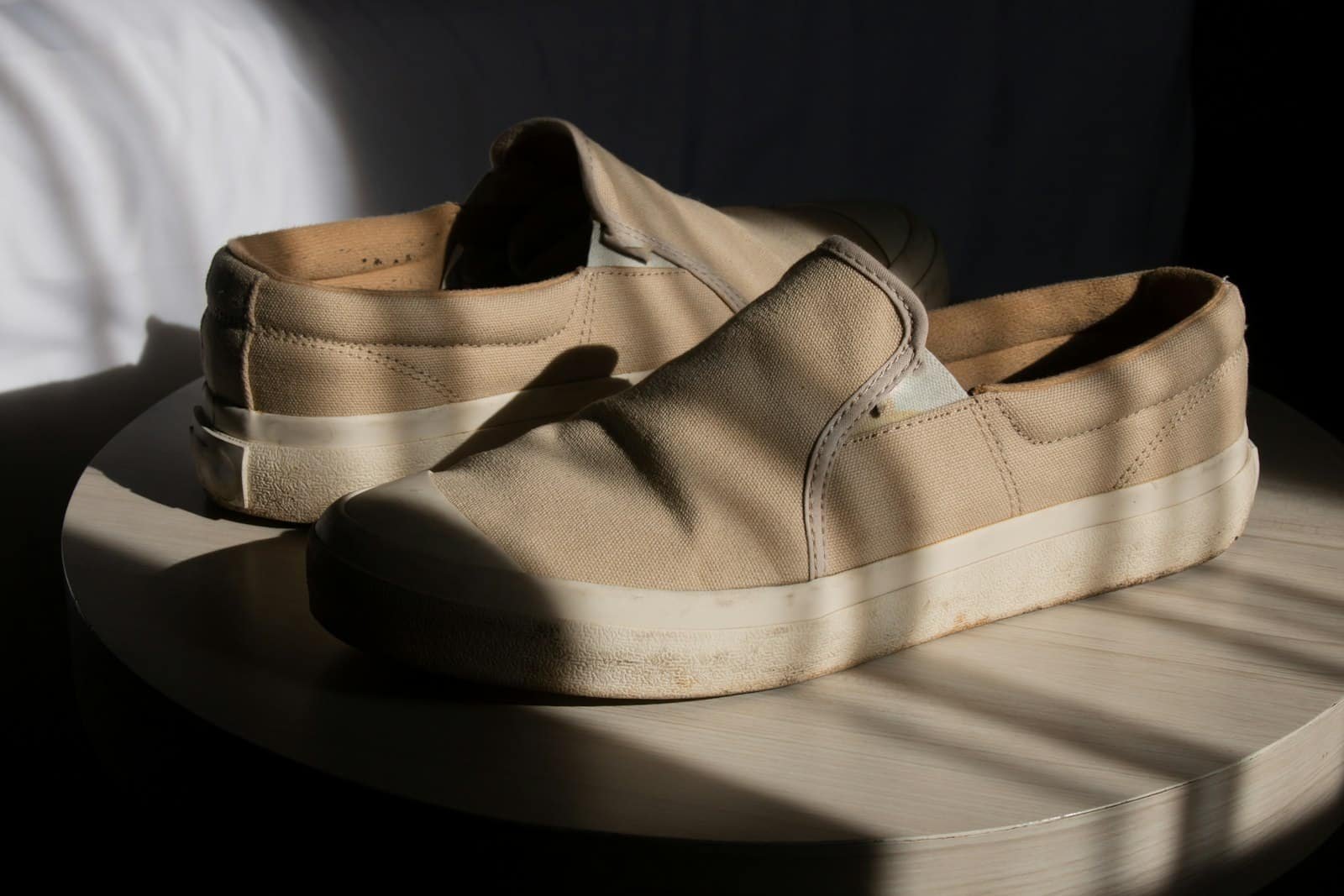 Pair of tan canvas slip-on shoes on a round table in sunlight