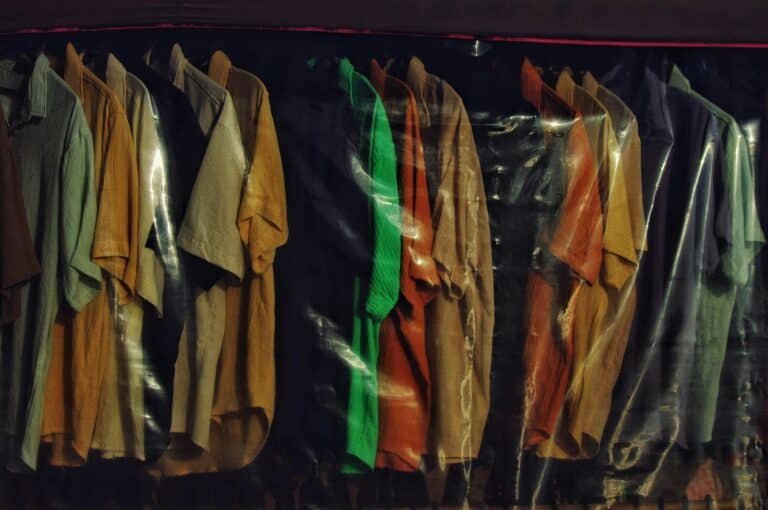 Rack of colorful short-sleeve shirts hanging behind a clear plastic cover