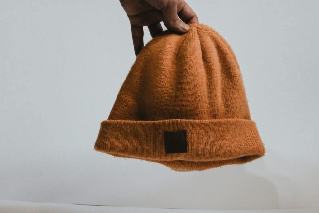 Hand holding a rust-brown knit beanie against a white background