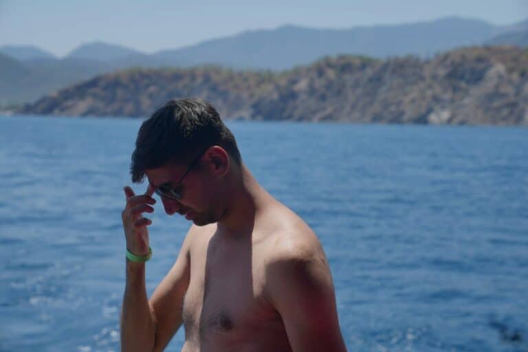 Shirtless man in sunglasses touching his hair by the sea