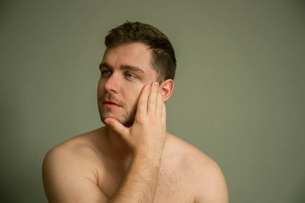 Shirtless man touching his cheek against a green background