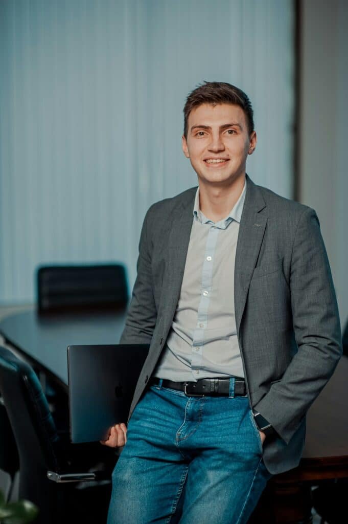 Smiling man in a grey blazer, light shirt and jeans in an office