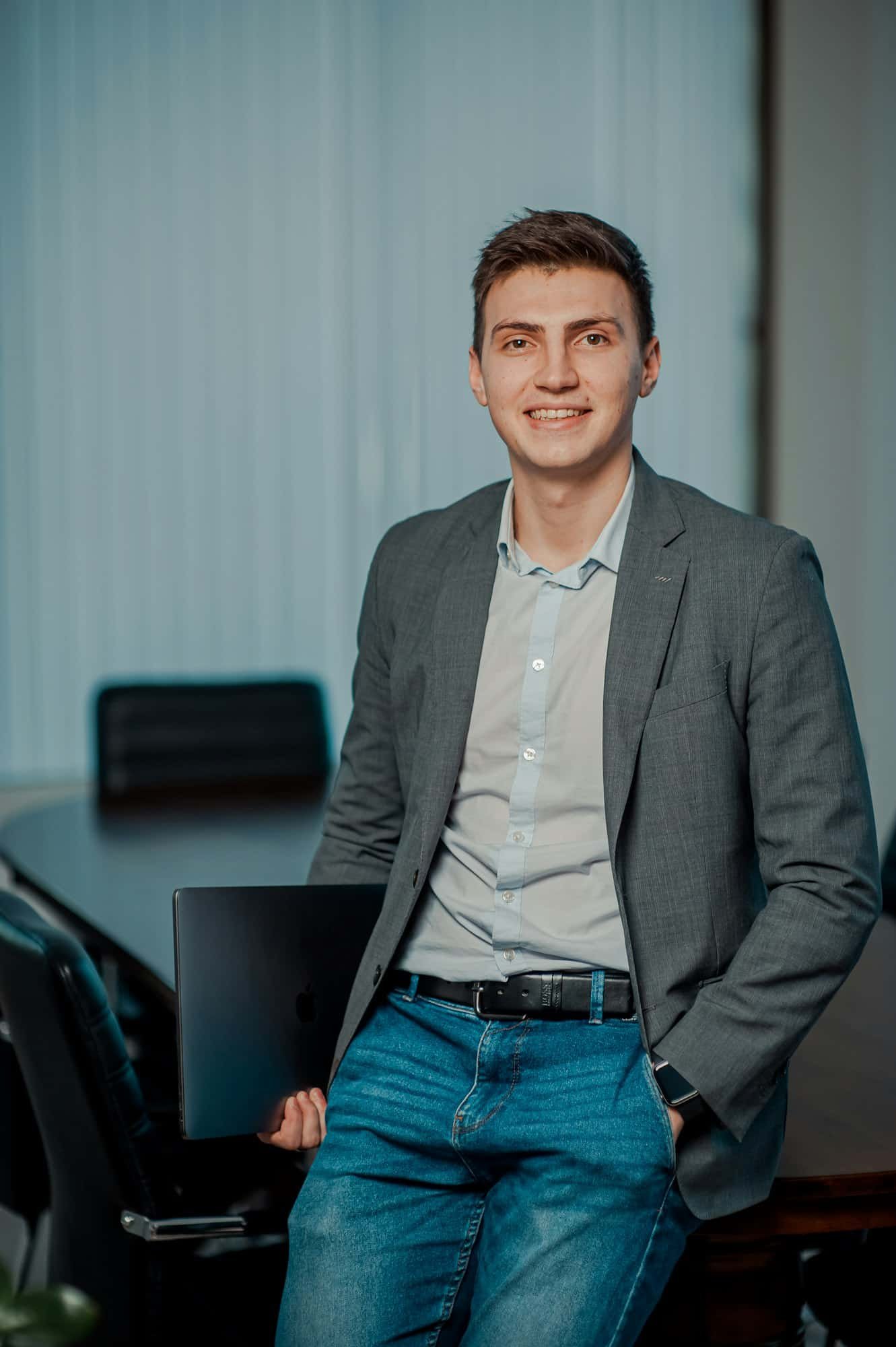 Smiling man in a grey blazer, light shirt and jeans in an office