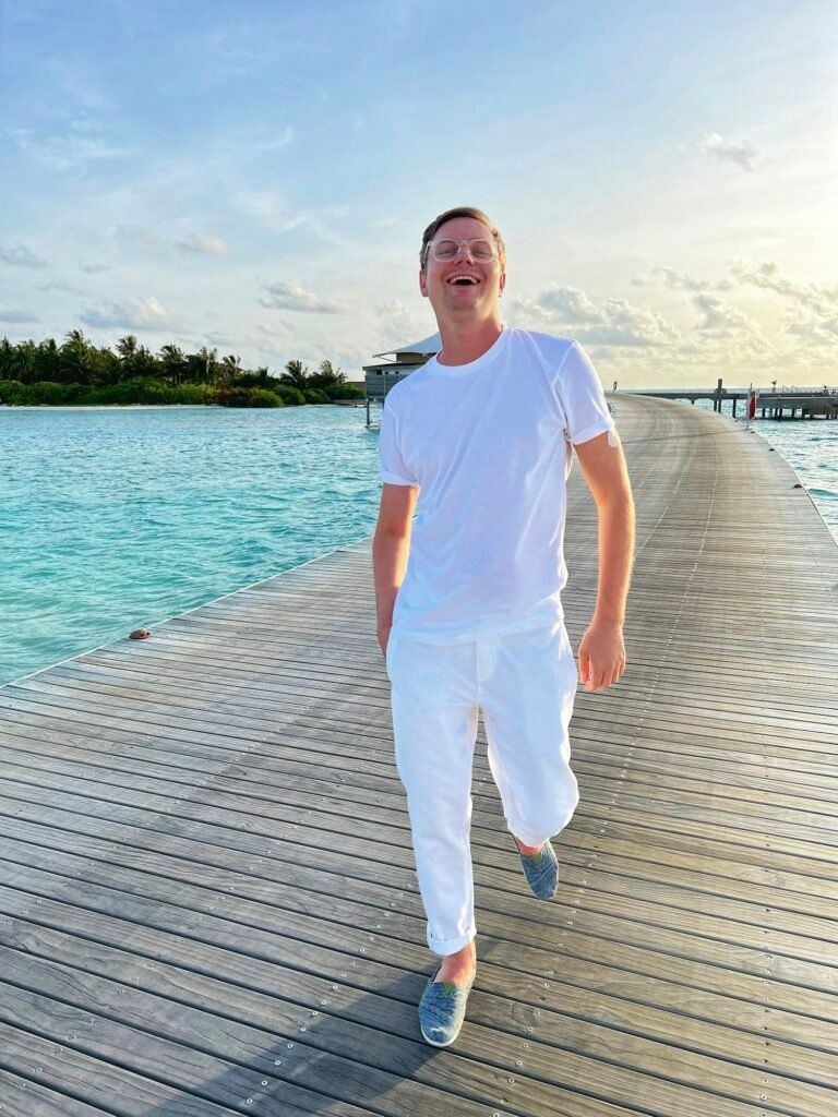 Smiling man in a white t-shirt and white trousers on a dock by the water