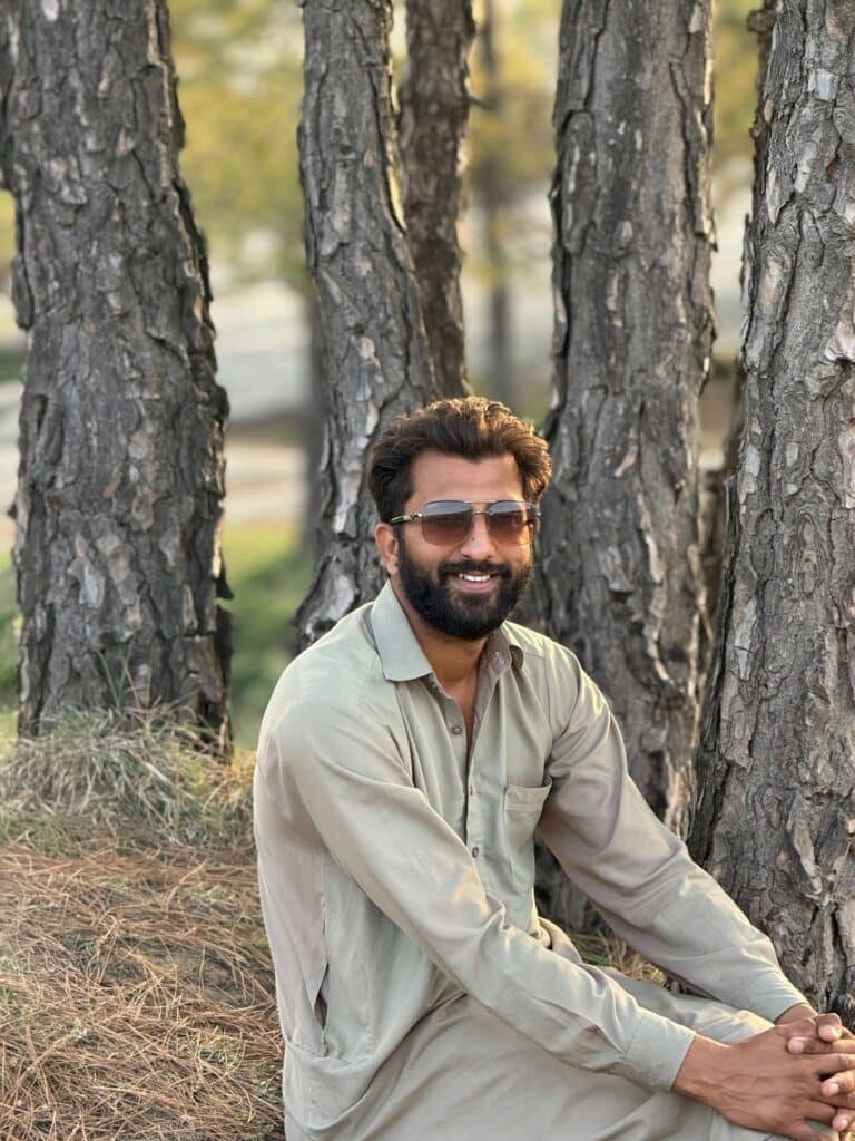Smiling man in sunglasses and a khaki shirt sitting among tree trunks