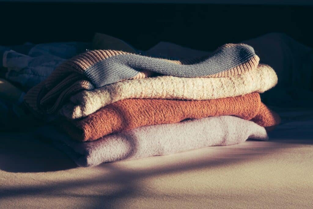 Stack of folded knit sweaters in cream, rust and brown