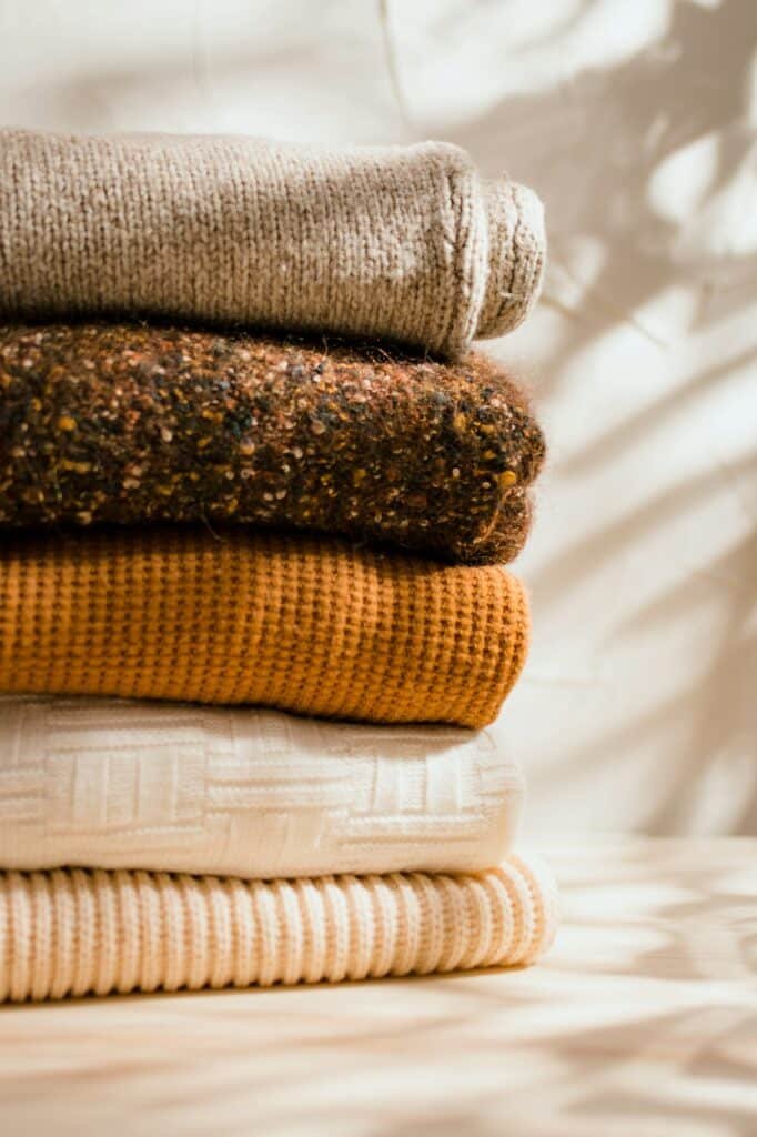 Tall stack of folded sweaters in oatmeal, brown, mustard and cream in warm light