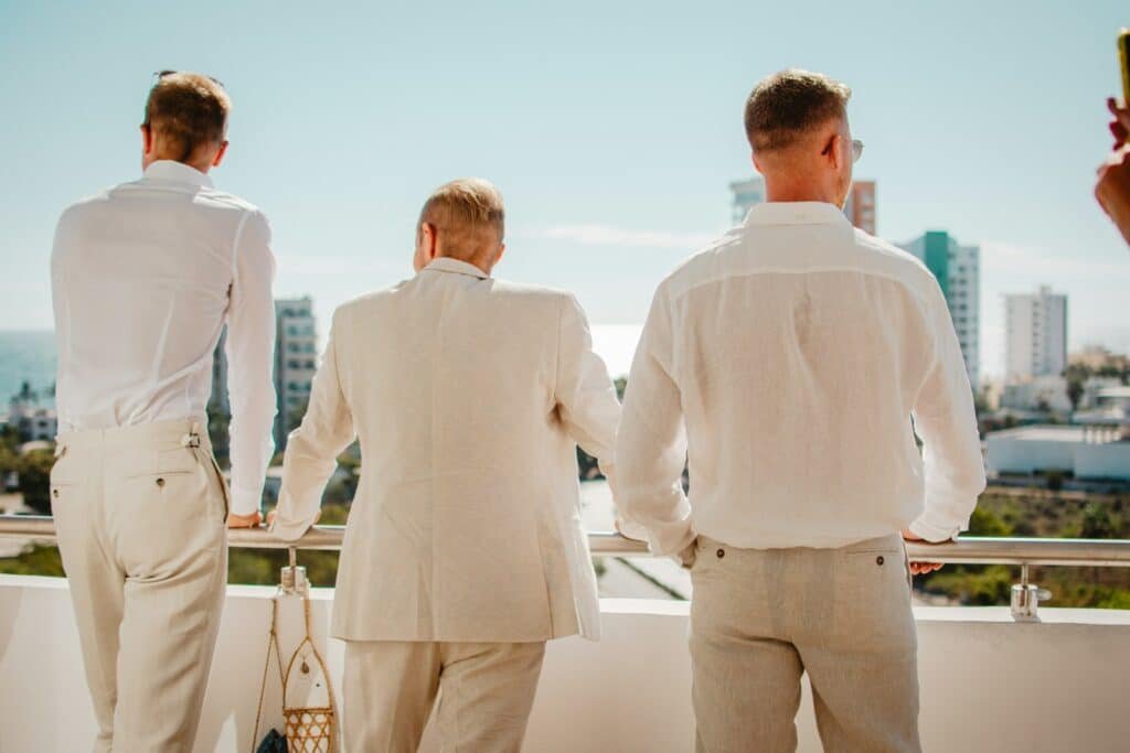 Three men in white and cream suits on a balcony overlooking a city