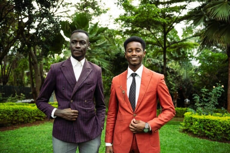Two men in tailored suits, one purple and one orange, standing in a garden