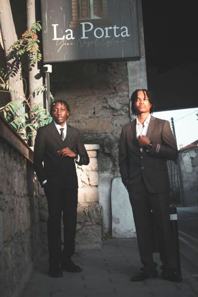 Two young men in dark suits standing outside a building