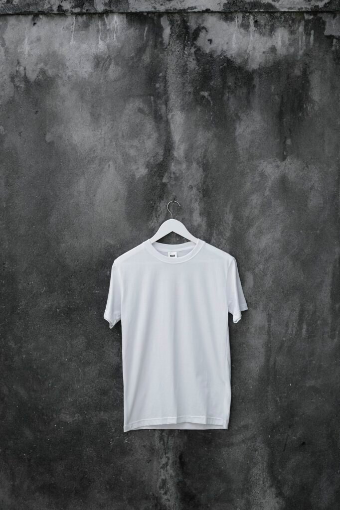Plain white crew neck t-shirt on a hanger against a grey concrete wall