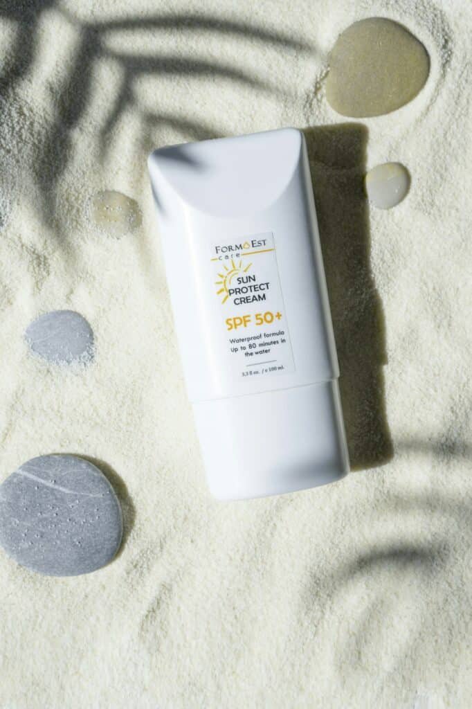 White SPF 50+ sun cream tube lying on sand