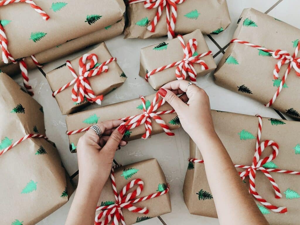 Hands tying red and white twine on small gifts wrapped in brown paper