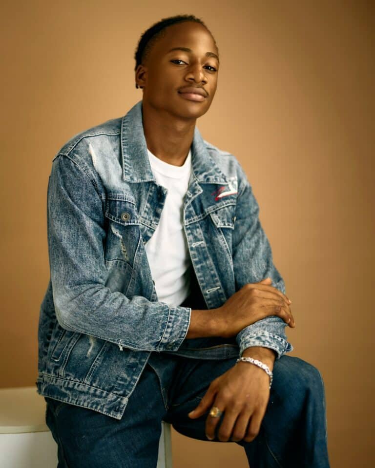 Young man in a denim jacket over a white t-shirt sitting on a stool