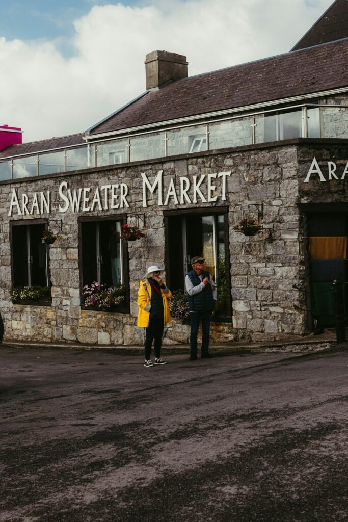 Two people standing outside the stone Aran Sweater Market building