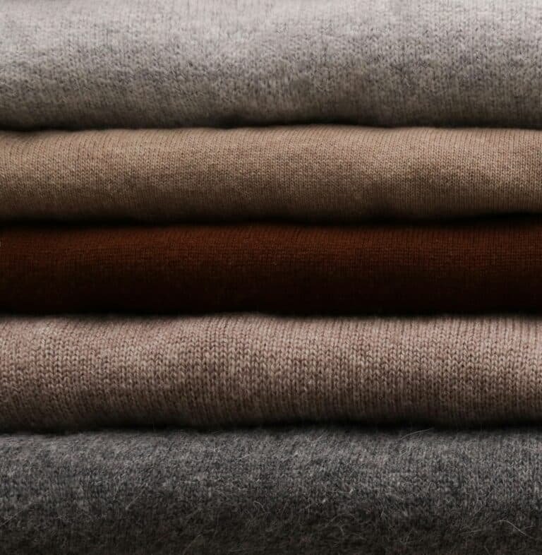 Stack of folded fine-knit sweaters in gray, taupe and brown
