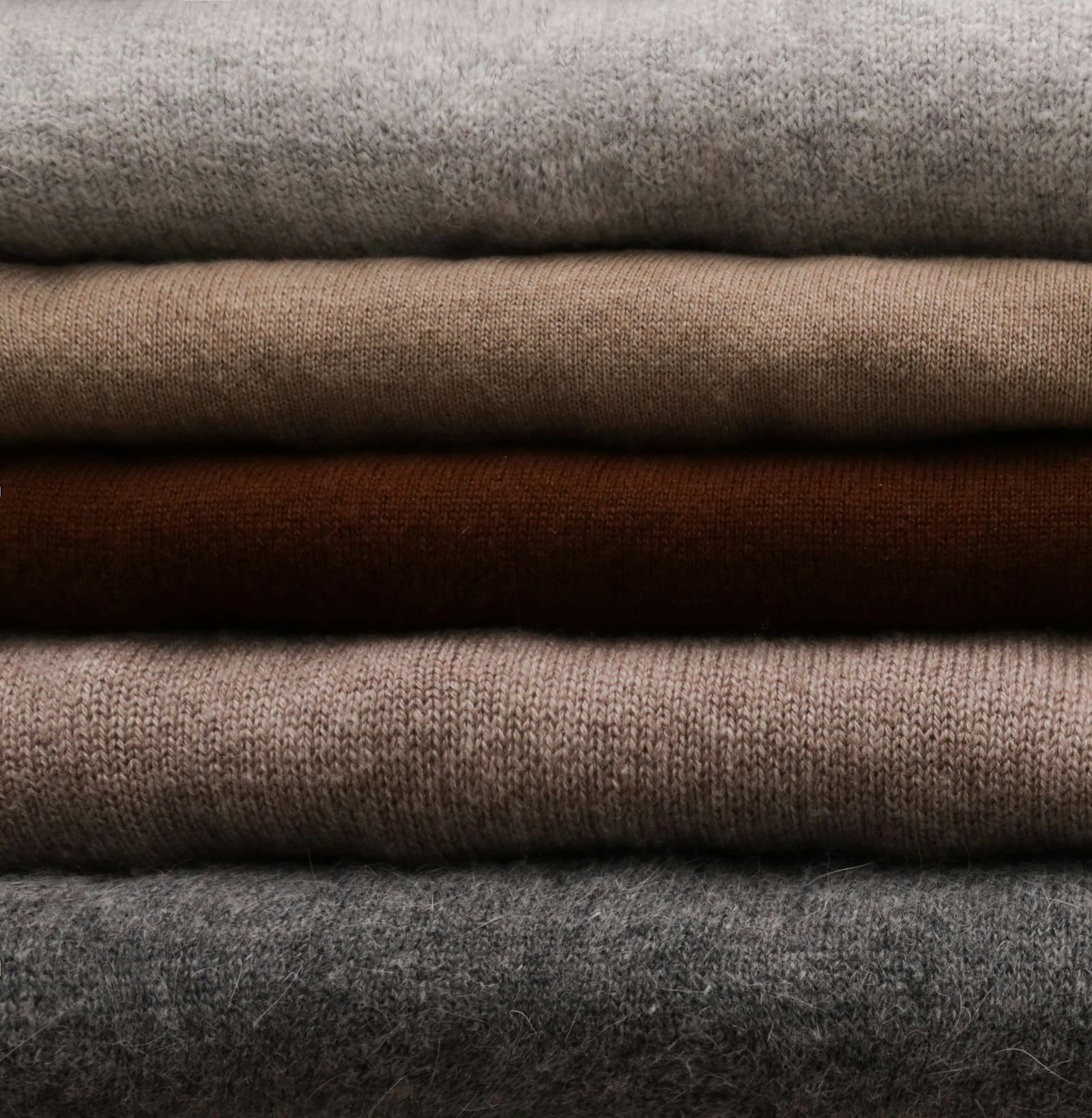 Stack of folded fine-knit sweaters in gray, taupe and brown