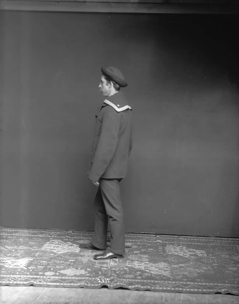 Black and white studio portrait of a young sailor in uniform and cap, seen in profile